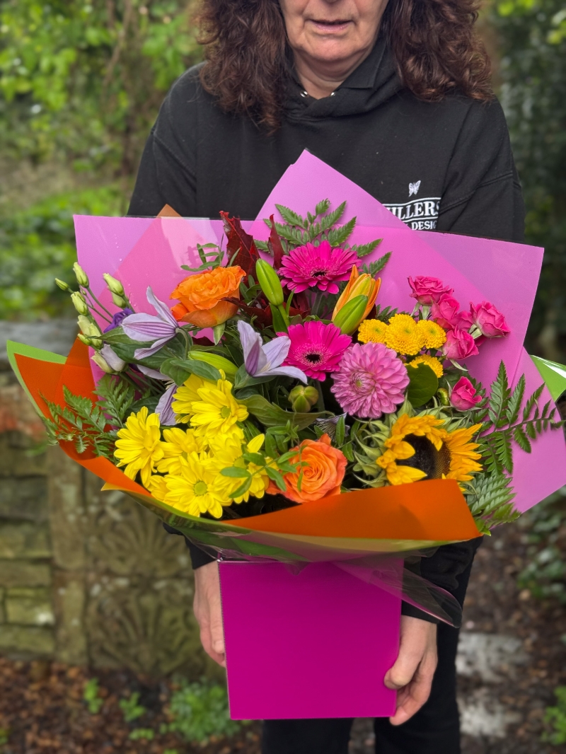 Colour Burst hand-tied bouquet with sunflowers, roses, germini, chrysanthemums and lilies in bright pink, orange and yellow tones