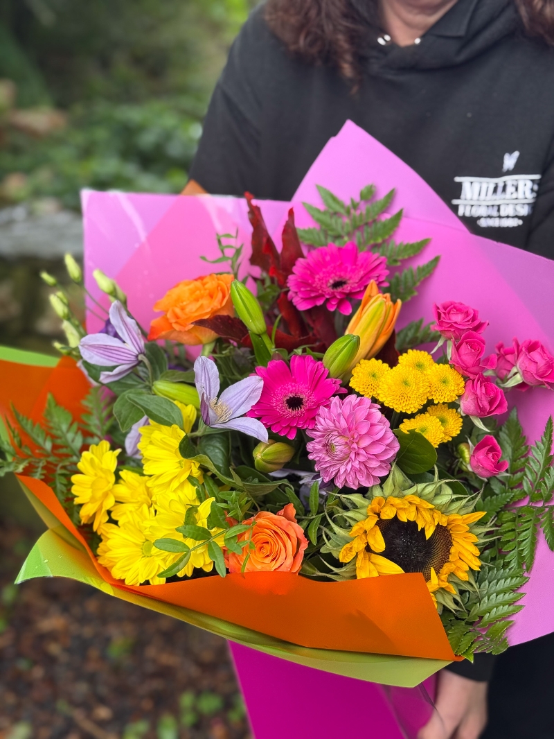 Colour Burst hand-tied bouquet with sunflowers, roses, germini, chrysanthemums and lilies in bright pink, orange and yellow tones
