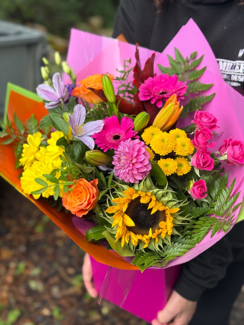 Colour Burst hand-tied bouquet with sunflowers, roses, germini, chrysanthemums and lilies in bright pink, orange and yellow tones
