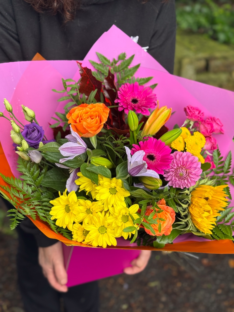 Colour Burst hand-tied bouquet with sunflowers, roses, germini, chrysanthemums and lilies in bright pink, orange and yellow tones