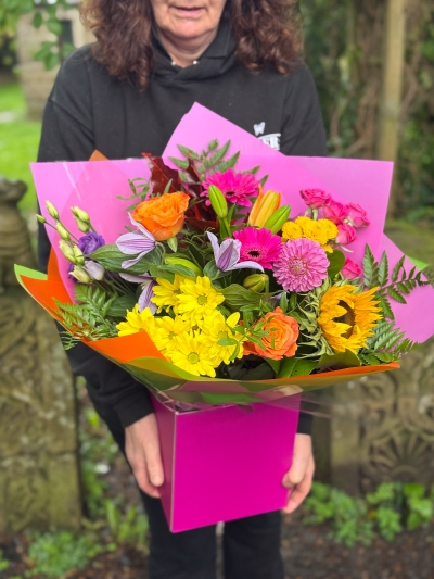 Colour Burst hand-tied bouquet with sunflowers, roses, germini, chrysanthemums and lilies in bright pink, orange and yellow tones