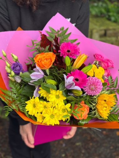 Colour Burst hand-tied bouquet with sunflowers, roses, germini, chrysanthemums and lilies in bright pink, orange and yellow tones
