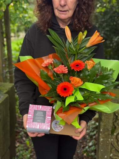 Petite bright flower gift box with orange lilies, germini, roses, carnations and fresh green foliage